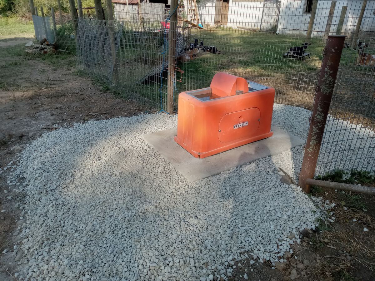A finished poly watering tank plumbed and set on a concrete pad with a gravel apron, inside a fenced working pen